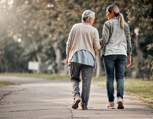 Eine ältere Frau und eine jüngere Frau gehen Hand in Hand einen Weg entlang.